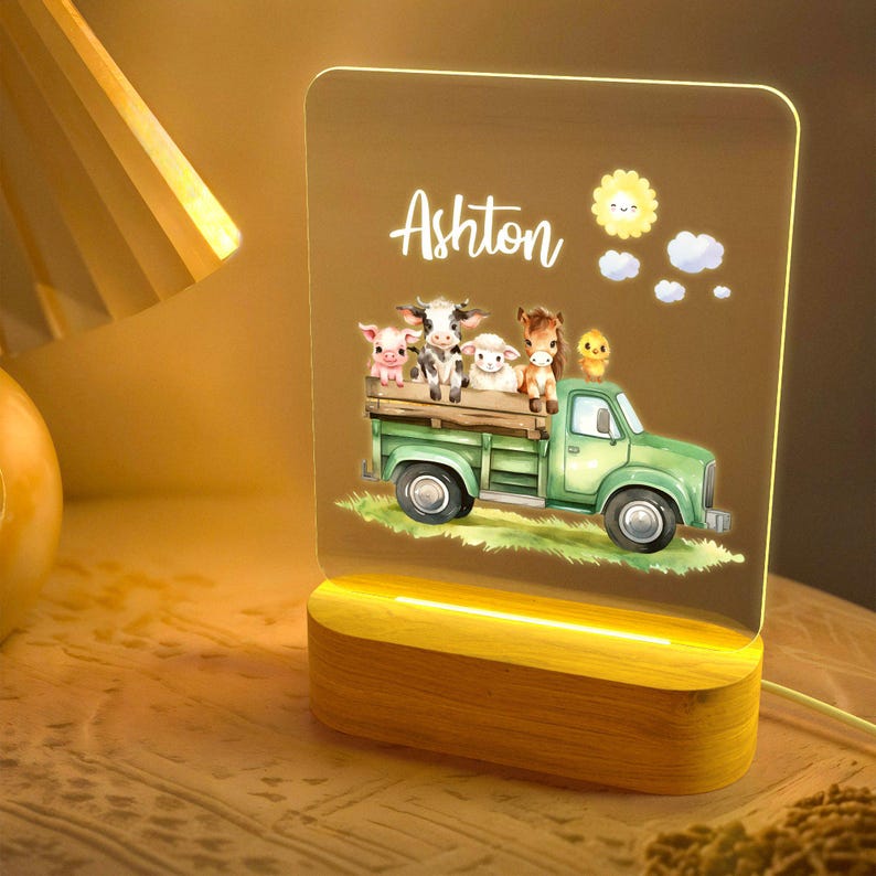 May include: A wooden night light with a clear acrylic panel featuring a green truck carrying farm animals. The panel is illuminated with a warm white light. The name Ashton is printed on the panel.