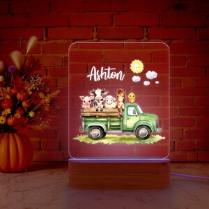 May include: A personalized night light with a wooden base. The light features a green truck with a white bed carrying a cow, pig, sheep, horse, and a chick. The text "Ashton" is displayed above the truck.