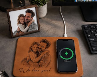 Pode incluir: Uma base de carregamento sem fios em pele castanha com uma ilustração gravada a laser de um homem e uma criança a abraçarem-se, com o texto "We love you!" por baixo. Um smartphone preto está colocado à direita com um ícone de carga verde.