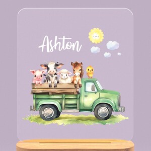 May include: A green toy truck with a white cab and a wooden bed. A pig, cow, lamb, and horse are sitting in the bed of the truck. A yellow chick is perched on the cab. The sun is shining in the sky above the truck. The name Ashton is written in white letters on a purple background.