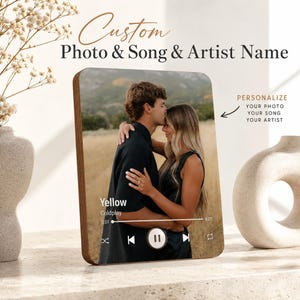 Op de afbeelding: Een rechthoekige houten plaat met een aangepaste foto van een koppel dat elkaar omhelst in een veld. De print bevat een muziekspeler-interface met de songtitel Yellow, artiest Coldplay, een voortgangsbalk en witte afspeelpictogrammen.