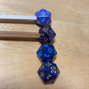 May include: Four purple and blue dice with gold and white numbers. The dice are arranged in a row from left to right, with the largest die on the left and the smallest die on the right.