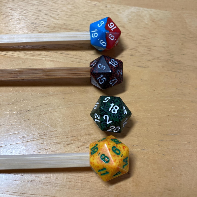 May include: Four different colored dice with white numbers on them are attached to wooden sticks. The dice are red and blue, brown and white, green and white, and yellow and orange.