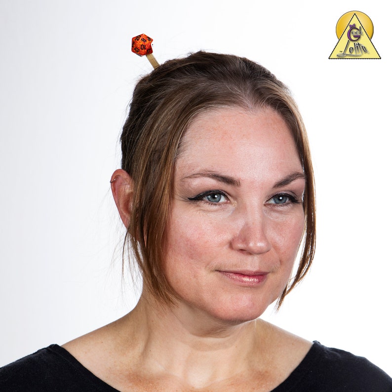 May include: A woman with brown hair wearing a black shirt has a red and black dice on a wooden stick in her hair.