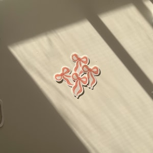 May include: Four pink and white bow stickers on a white surface.