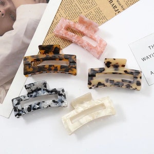 May include: Set of five hair clips in various colours and patterns. The clips are made of plastic and have a rectangular shape with a curved top. The patterns include leopard print, black and white marble, and pink and white marble.