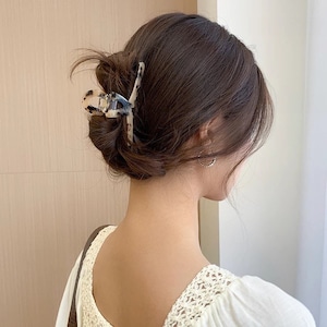 May include: A brown and white patterned hair claw clip with a tortoiseshell design. The clip is holding a woman's hair in a bun.