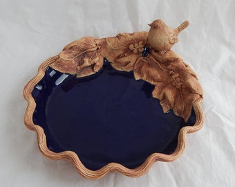 Handcrafted stoneware round basket dish with grape leaves and bird in blue glaze.