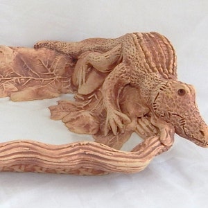 May include: A ceramic serving dish shaped like a log with a white glazed interior. The dish is decorated with a sculpted alligator and leaves on the sides.
