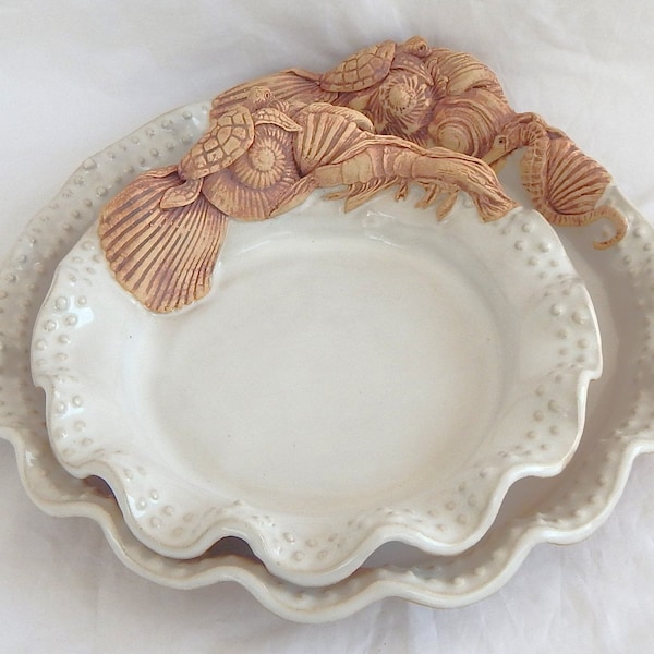 Handcrafted stoneware bread and dinner plates, beaded with shells and other sea creatures in white glaze.