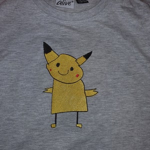 Puede incluir: Una camiseta gris con un personaje de dibujos animados bordado en amarillo. El personaje tiene orejas negras y una cola negra. El personaje tiene una sonrisa roja y mejillas rojas. La camiseta tiene una etiqueta que dice "alive" en ella.