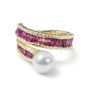 May include: A gold-toned ring with a spiral design, featuring a row of pink gemstones and a large white pearl. The ring has a textured band and a polished finish, showcasing a luxurious aesthetic.