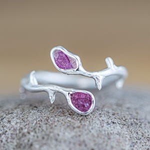 May include: A silver ring with a delicate branch design featuring two pink gemstones. The ring is open and adjustable.