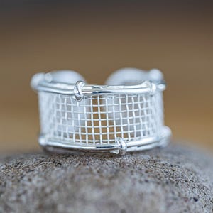 May include: A silver ring with a mesh design. The ring is made of a single piece of wire that is woven into a mesh pattern. The ring is a simple and elegant design.