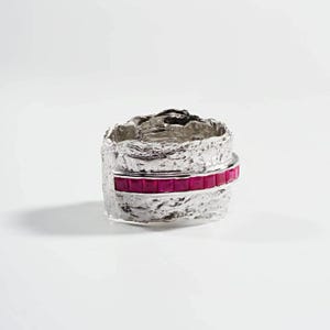 May include: A silver ring with a textured band and a single row of red ruby stones.