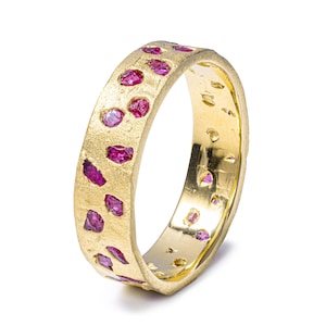 May include: A gold ring with a textured finish, set with irregularly shaped, vivid pink gemstones. The ring's design incorporates the gemstones into the band, creating a unique and eye-catching piece of jewellery.