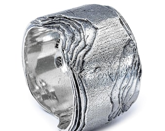 May include: A wide, textured silver ring with a unique, layered design. The ring has a rough, organic appearance, with visible details and a polished interior. The ring is marked with "925" indicating the silver content.