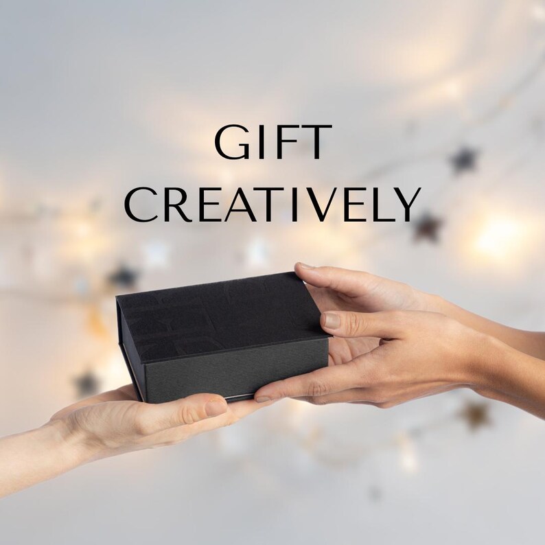May include: A black rectangular gift box is being exchanged between two individuals. The text on the image reads, 'GIFT CREATIVELY'.