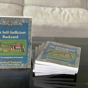May include: A stack of blue and gold books titled "The Self-Sufficient Backyard" for the independent homesteader by Ron and Johanna Melchiore.