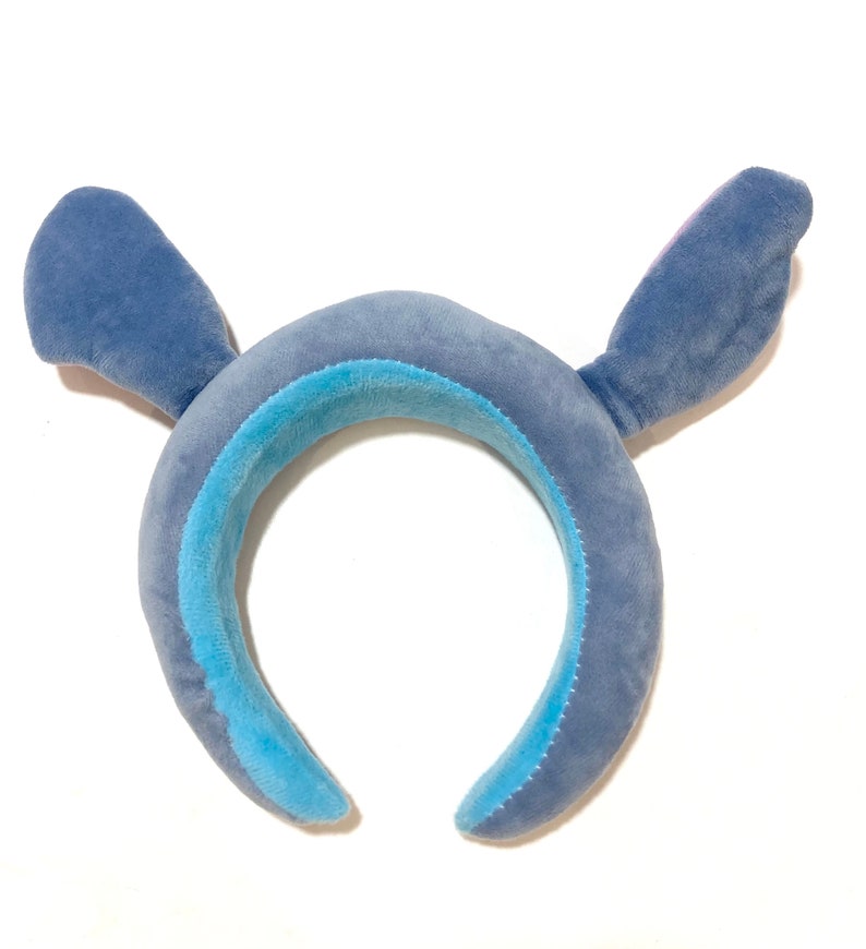 May include: Blue plush headband with large ears, resembling a cartoon character. The headband is made of soft, fuzzy fabric.