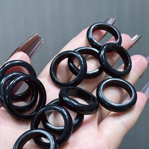 May include: A collection of black rings with a glossy finish. The rings are round and appear to be made of a solid, dark material. The rings are displayed on a light background.