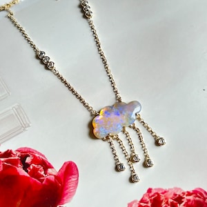 Könnte beinhalten: Eine goldene Kettenkette mit einem wolkenförmigen Opal-Anhänger und baumelnden Diamant-Akzenten. Der Opal ist schillernd in Blautönen, Grün- und Rosatönen.