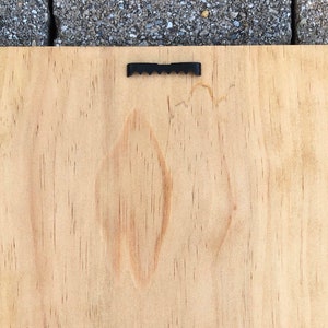 May include: A plain, light brown wooden sign with a black metal hanging hook on the top.