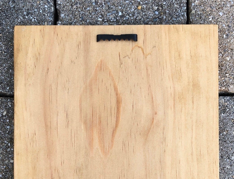 May include: A plain, light brown wooden sign with a black metal hanging hook on the top.