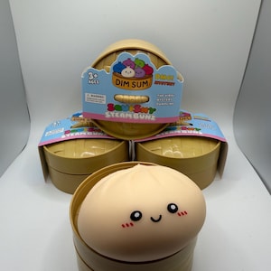 May include: A collection of Squishy Steam Bunz mystery toys. The packaging features a tan bamboo steamer design with the words "Dim Sum" and "Squishy Steam Bunz". The toy itself is a tan dumpling with a smiling face.