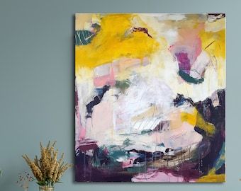 Op de afbeelding: Abstract schilderij met gele, roze, witte en paarse tinten. Het schilderij is op canvas en heeft een textuur. Het hangt aan een blauwe muur boven een houten plank.