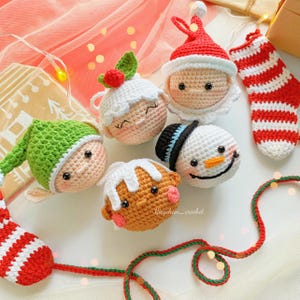 May include: A collection of handmade crochet Christmas ornaments, including Santa Claus, a snowman, an elf, a gingerbread man, and a Christmas pudding. The ornaments are in red, white, green, and brown. A red and white striped stocking is also present.
