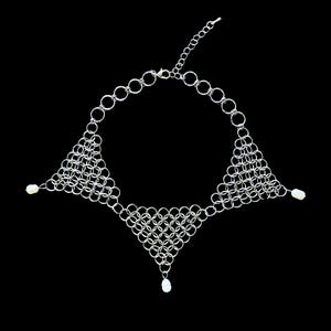 May include: A silver-toned chainmail necklace featuring three triangular woven metal mesh sections connected by a circular link chain. The necklace is accented with three small, white, oval-shaped beads attached to the outer points of the mesh.
