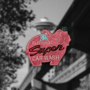 May include: Embroidered patch featuring a pink elephant with the words "Elephant Super Car Wash" in a retro style. The elephant is holding a blue washcloth. The patch has a black border and a green hat.