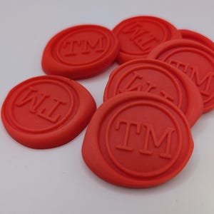May include: Six red wax seals with the letters "TM" embossed on them. The seals are arranged in a semi-circle.