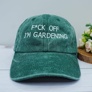 Peut inclure: Casquette de baseball verte avec le texte brodé en blanc "F*CK OFF I'M GARDENING". La casquette a une visière incurvée et un aspect légèrement délavé. C'est un accessoire décontracté.