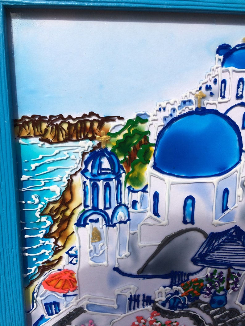 Puede incluir: Una pintura de un edificio blanco con un techo abovedado azul, sobre un fondo de mar azul y un acantilado rocoso. El edificio est&aacute; rodeado de otros edificios blancos y una colina verde. La pintura est&aacute; enmarcada en un marco azul.