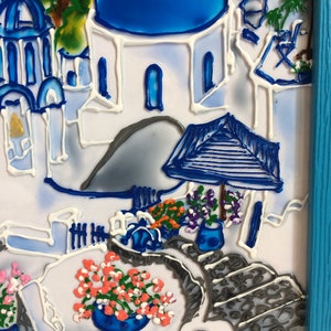 Puede incluir: Una obra de arte de vidrio pintado que representa un edificio blanco con una c&uacute;pula azul, rodeado de flores y un camino de piedra gris. La obra est&aacute; enmarcada en un marco azul.