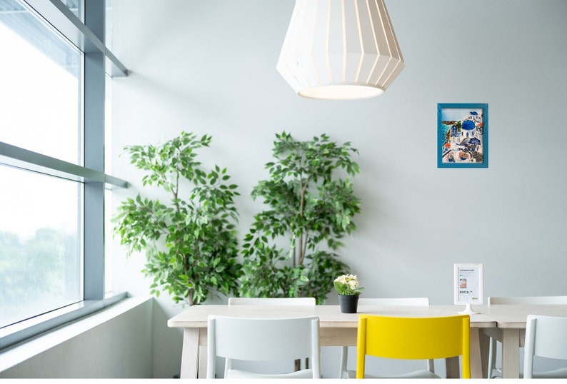 Puede incluir: Una mesa de comedor blanca con cuatro sillas, dos blancas y dos amarillas. Hay dos plantas en macetas, un cuadro enmarcado de un pueblo griego y un cartel con el texto "Lemonade" en la mesa. La habitaci&oacute;n tiene una ventana grande y una l&aacute;mpara de techo blanca.