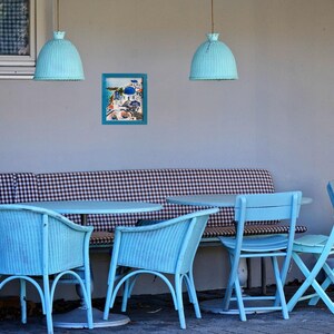 Puede incluir: Un banco de cuadros azules y blancos con cuatro sillas azules y una mesa azul. Dos l&aacute;mparas colgantes azules cuelgan sobre la mesa. Un cuadro enmarcado de una escena de playa cuelga en la pared.