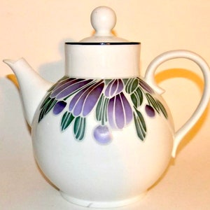 May include: White teapot with a floral design featuring purple and green flowers. The teapot has a round body and a lid with a knob.