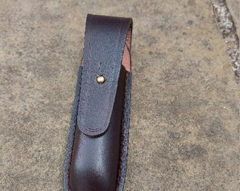 May include: A brown leather sheath with a brass button closure. The sheath is designed to hold a small knife or tool.