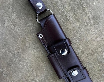 May include: A brown leather knife sheath with a belt loop and snap closure. The sheath has silver rivets and stitching.