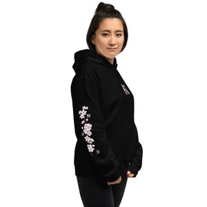 May include: Black hooded sweatshirt with a floral design on the sleeve. The design features pink cherry blossoms and Japanese characters.