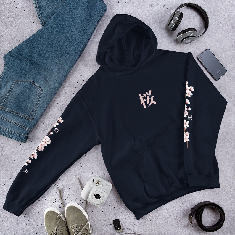 May include: A navy blue hoodie with a pink Japanese character on the front and a floral design on the sleeves. The floral design features pink blossoms and green leaves.