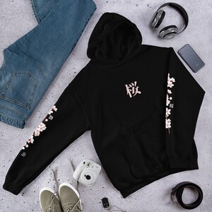 May include: Black hooded sweatshirt with a pink Japanese character on the front and pink cherry blossoms on the sleeves. The character is "桜" which means "cherry blossom".