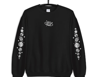 Peut inclure: Sweat-shirt noir avec un motif blanc du système solaire sur le devant et les manches. Le motif comprend des planètes, des étoiles et une planète avec des anneaux.