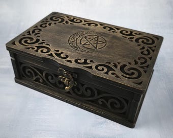 May include: A dark brown wooden box with intricate carved designs. The lid features a crescent moon and a pentagram. The box has a metal clasp and is likely used for storing small items. The overall aesthetic is gothic or mystical.