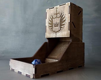 May include: A wooden dice tower with a carved design of a shield with a crown and sword. The tower has a slot for dice to roll out of. A blue die is in the bottom of the tower.