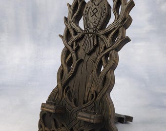 May include: A dark brown wooden phone stand featuring a laser-cut design of a raven perched on a branch. The stand includes intricate tree branch patterns, a central rune symbol on the bird's chest, and a woven knotwork base with two supports.