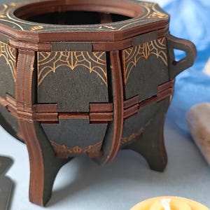 Mystical wooden witch cauldron box with engraved arcane symbols, handcrafted Wiccan trinket holder, gothic altar decor for storing runes, jewelry, and sacred items, enchanted fantasy storage chest, aged wood design with dark academia aesthetic, perfect for Halloween witchcraft decor, handcrafted wooden potion storage, mystical home accent for Wiccans and pagans, rustic fantasy-inspired keepsake box, spell jar organizer, unique handcrafted witchy home decor piece